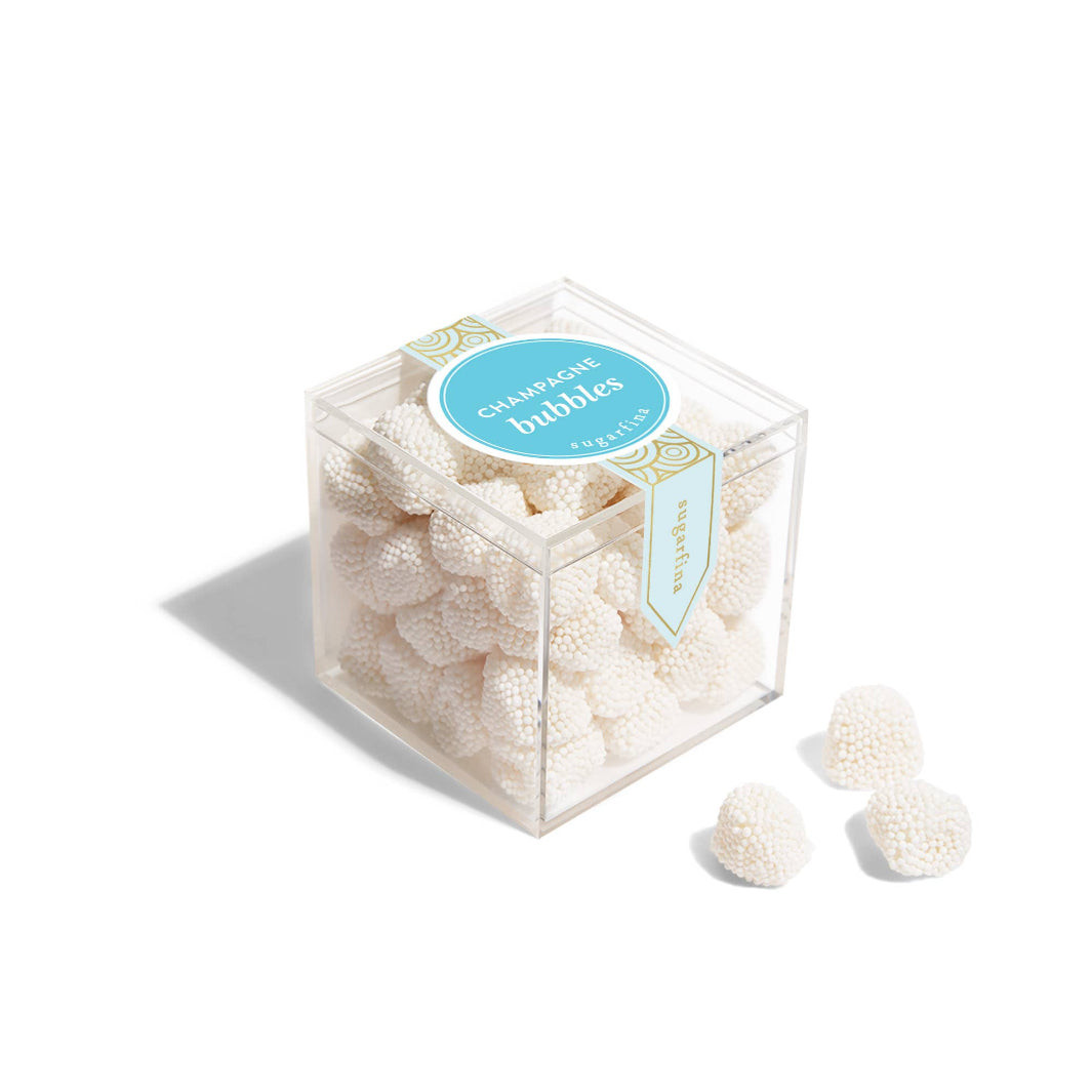 Champagne-flavored gummy candies dressed in tiny white nonpareils, packaged in a clear box—elegant and sweet treats for gifting and celebrations.