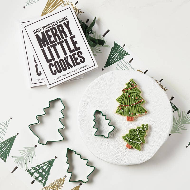 Christmas tree cookie cutters on a serving board with two Christmas tree decorated cookies.