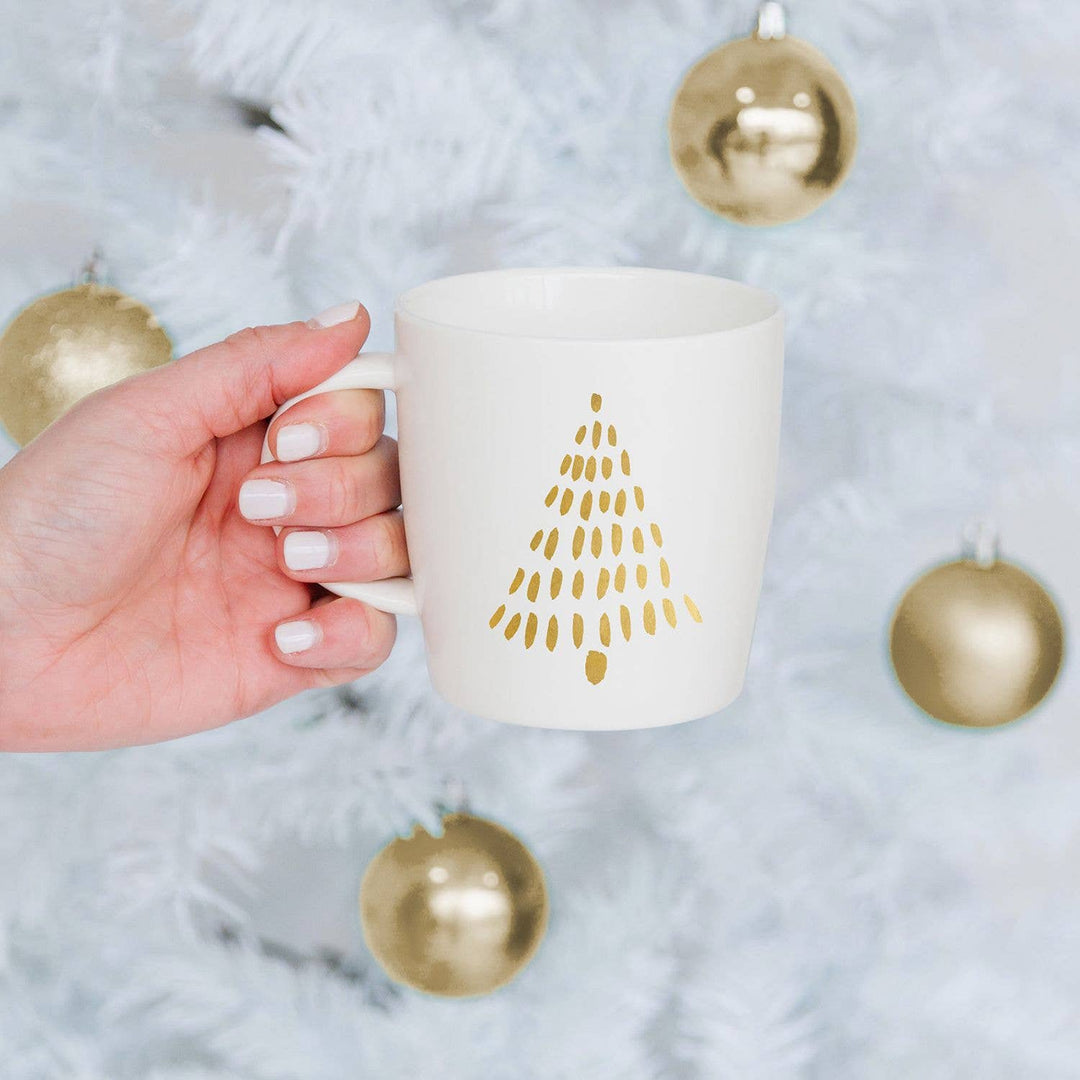 Gold Christmas Tree Mug being held with a white tree branches and ornaments in the background. 