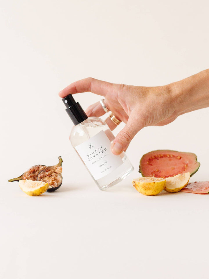 A hand holding the Guava Fig Room + Linen Spray, misting for a fresh scent.