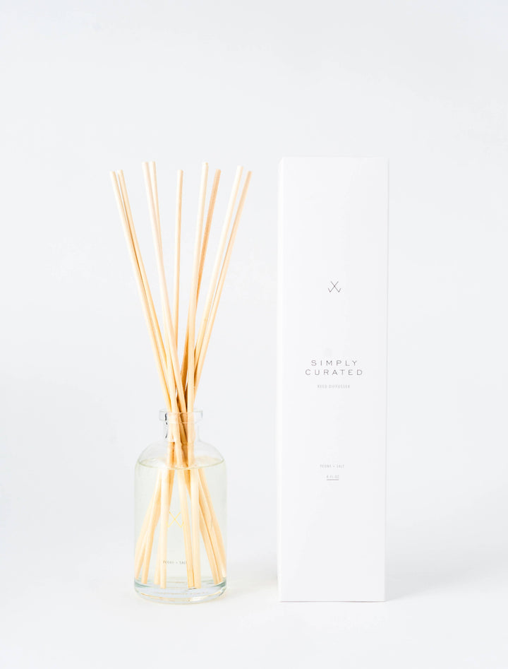 Guava Fig Reed Diffuser in a glass bottle with natural rattan reeds next to its clean and modern packaging.