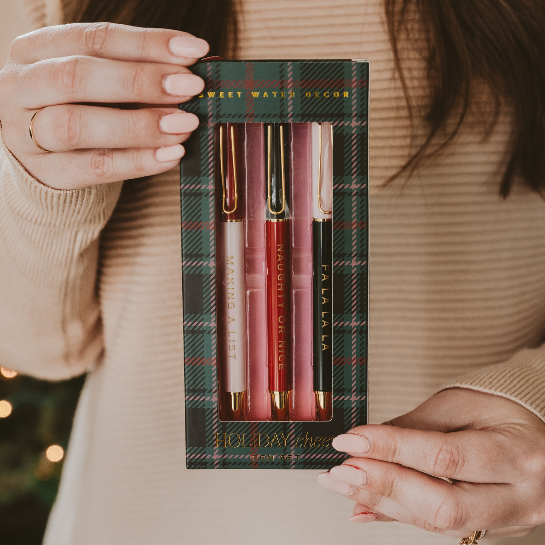 Close-up of Christmas pens with gold accents and holiday phrases: "Making A List," "Naughty or Nice," "Fa La La La.