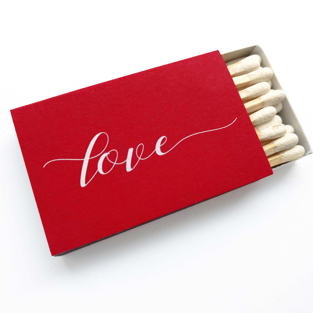 An open Love Matches box revealing neatly arranged white-tipped matchsticks inside the ruby red case.