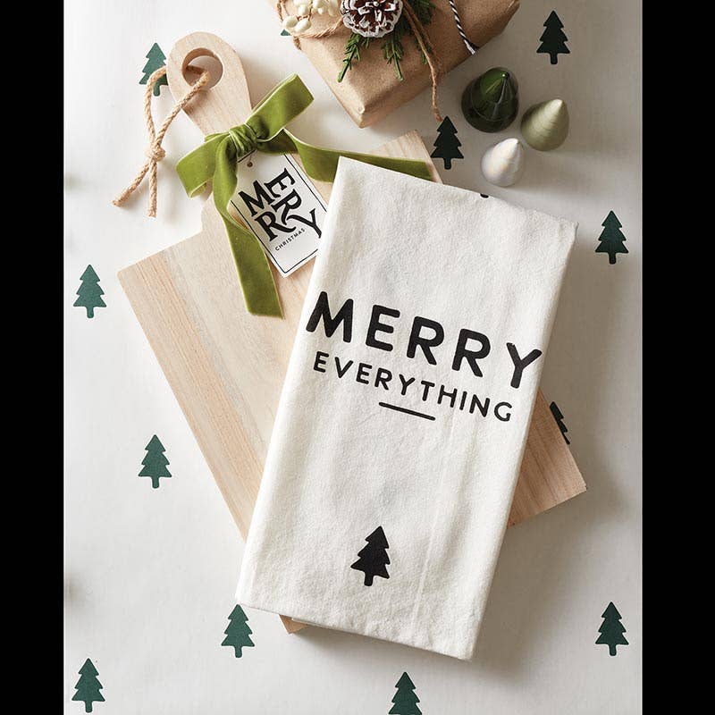 White tea towel with "Merry Everything" text, displayed in a festive kitchen setting as part of holiday decor.