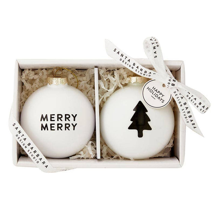 Two glass ornaments, one with “Merry Merry” in black lettering and the other with a black tree design, presented in an elegant gift box.