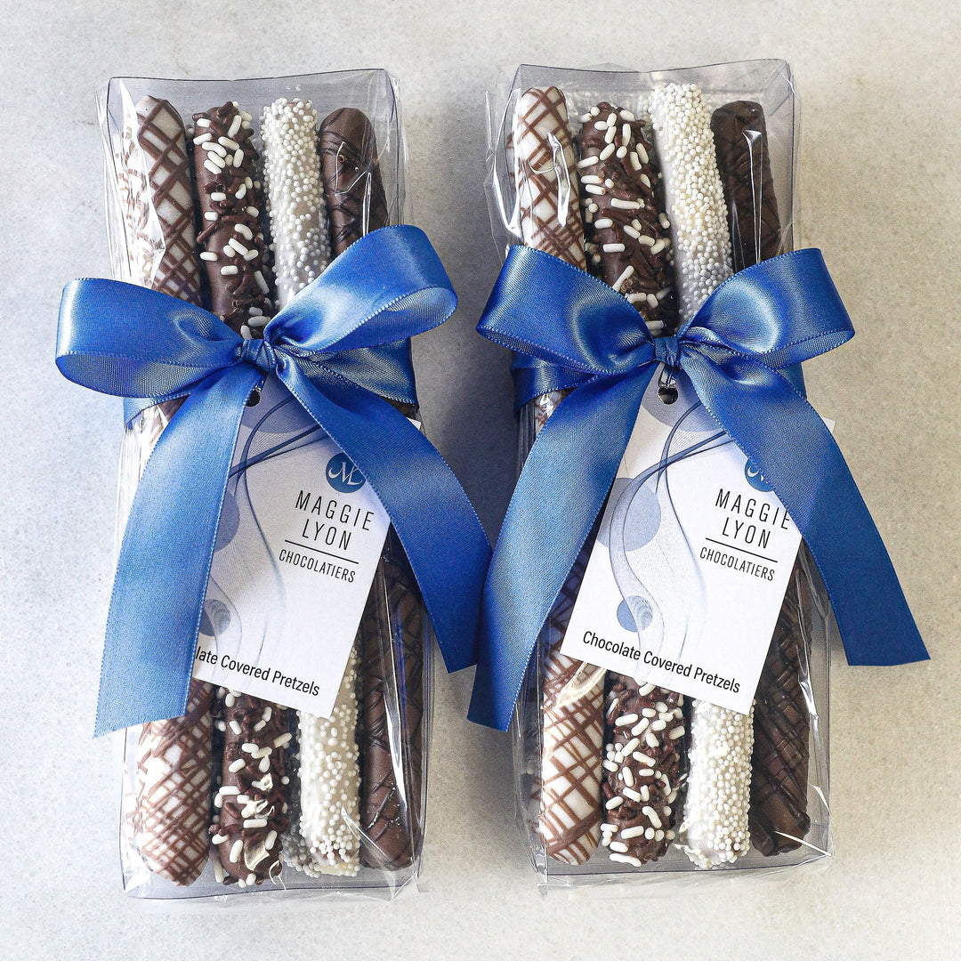 Milk & White Chocolate Pretzel Rods, decorated with chocolate drizzle, nonpareils, and jimmies, displayed in holiday packaging.