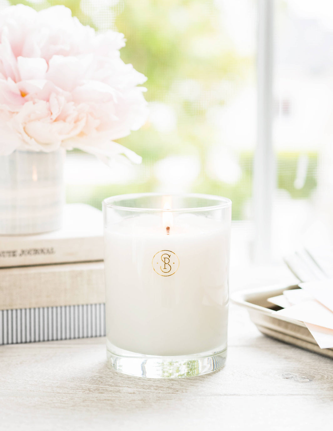 Pink Petal Candle on a desk next to books and pink flowers.