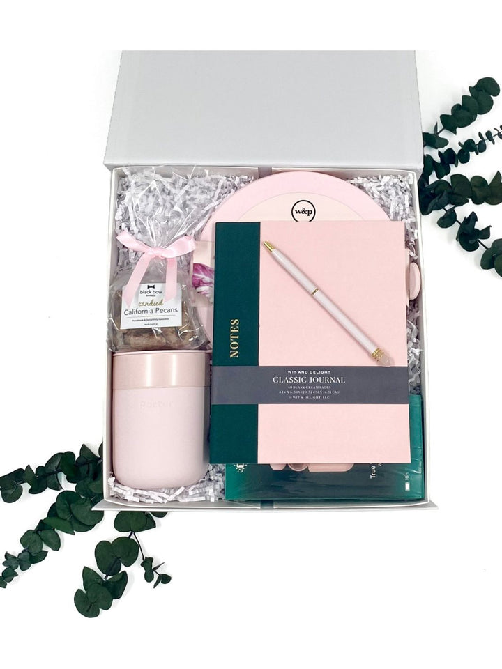 Pretty in Pink Essentials Gift Box featuring a pink notebook, crystal pen, earbuds, ceramic mug, lunch bowl, and candied pecans.