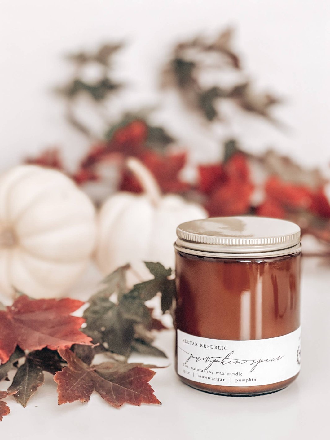 Pumpkin Spice Soy Wax Candle with leaves and pumpkins in the background, perfect for fall and Thanksgiving.