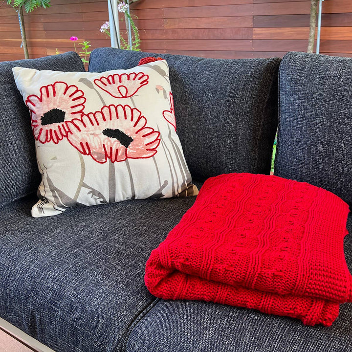 Cozy red cable knit throw blanket folded on a couch, perfect for home decor.