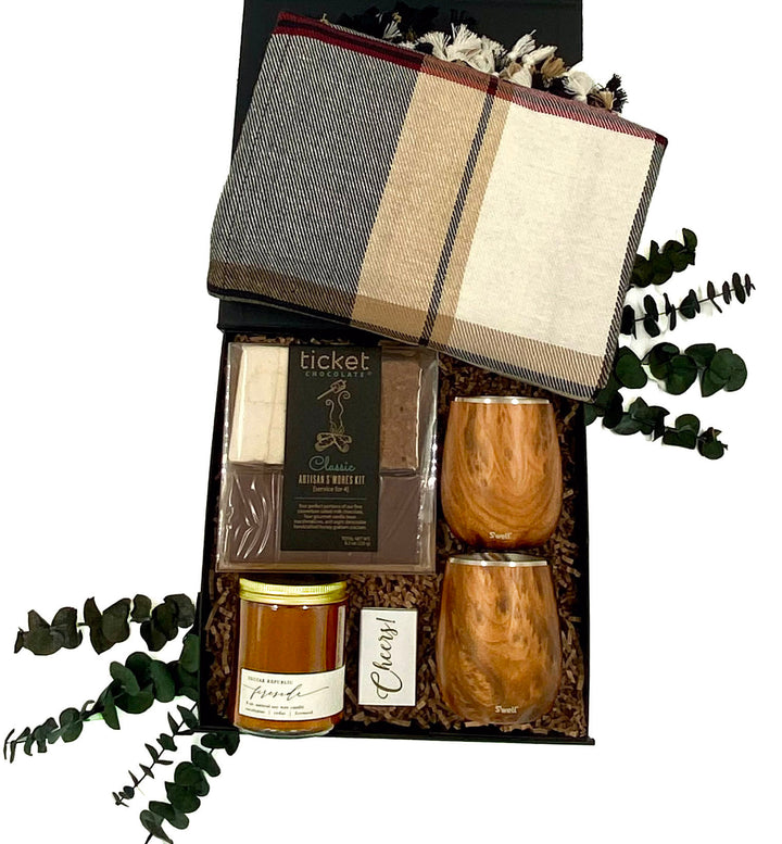 S’mores and Sip Gift Box featuring two Teakwood wine tumblers, plaid throw blanket, Fireside soy candle, Artisan S’mores Kit, and Cheers matchbook for a romantic and cozy night.