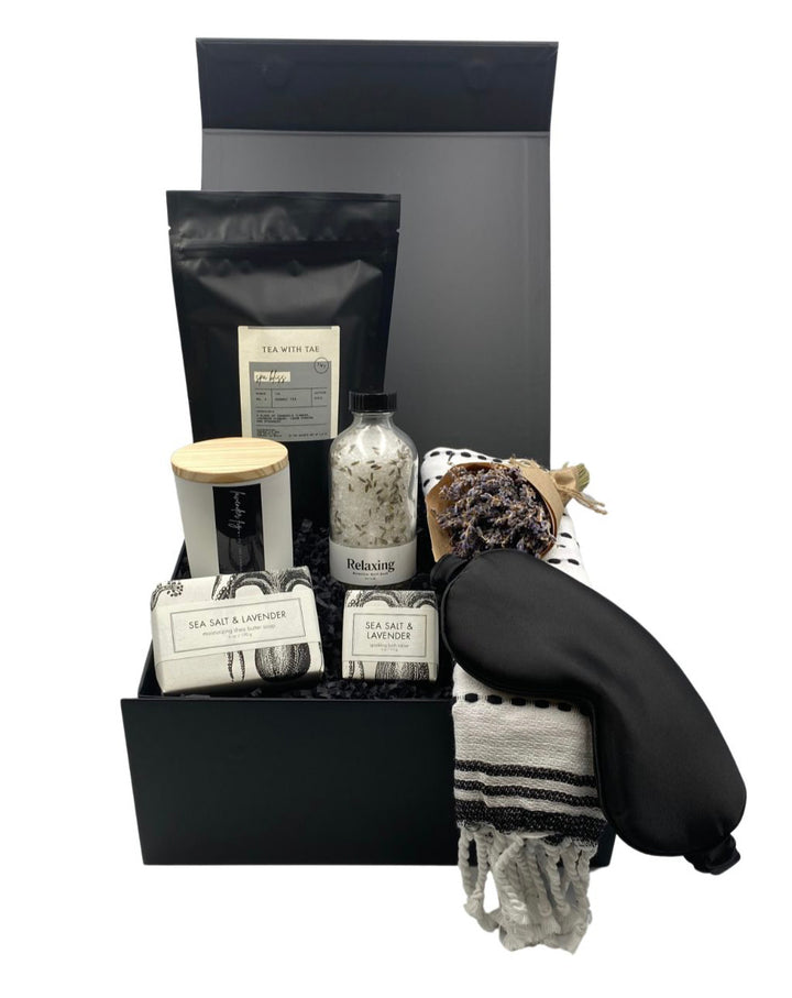 Spa Bliss Gift Box featuring a relaxing botanical bath soak, lavender fig candle, sea salt & lavender shea butter soap, bath tablet, Spa Bliss tea, black silk sleep mask, elegant guest towel, and a petite French lavender bundle. Ideal for spa gift sets, self-care gift baskets, and relaxation gifts.