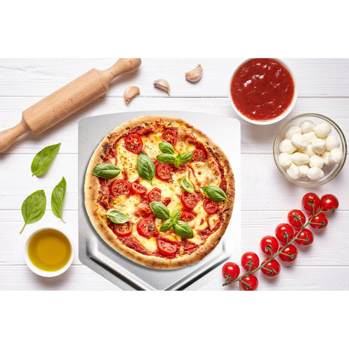 Outset Stainless Steel Pizza Paddle with pizza and ingredients on a table.